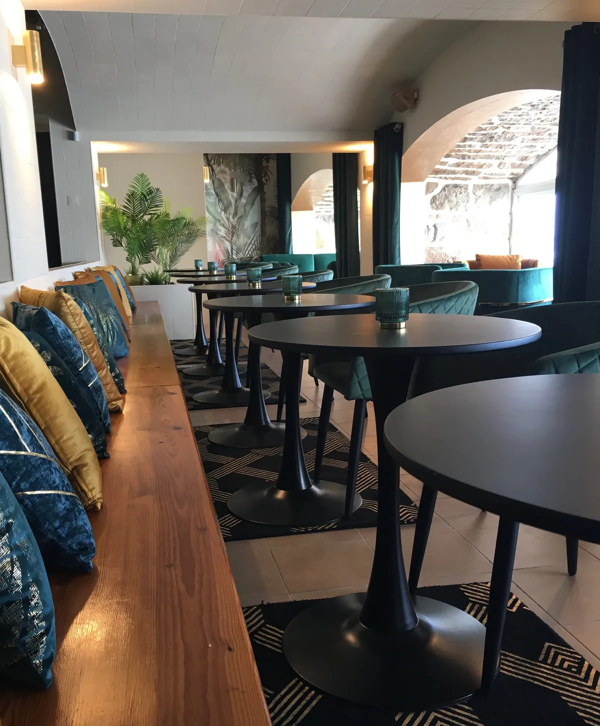 Banquette en bois garnie de coussins bleus et moutarde, le long des tables