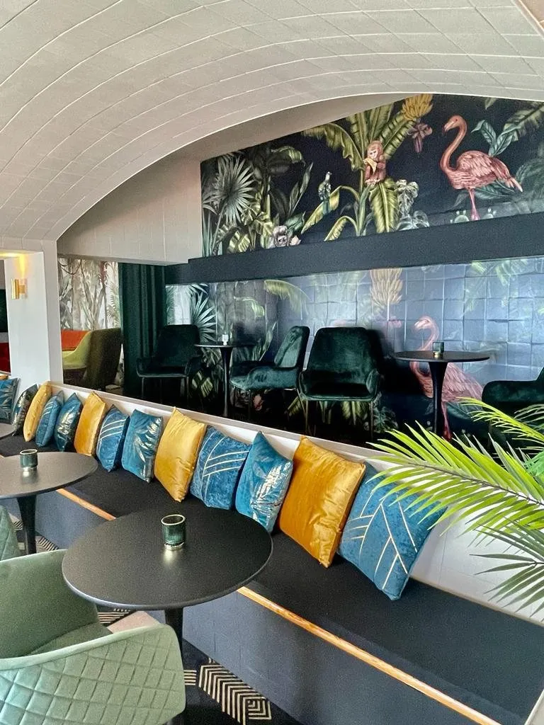 Longue banquette aux coussins bleus et moutarde, papier peint jungle en fond de salle