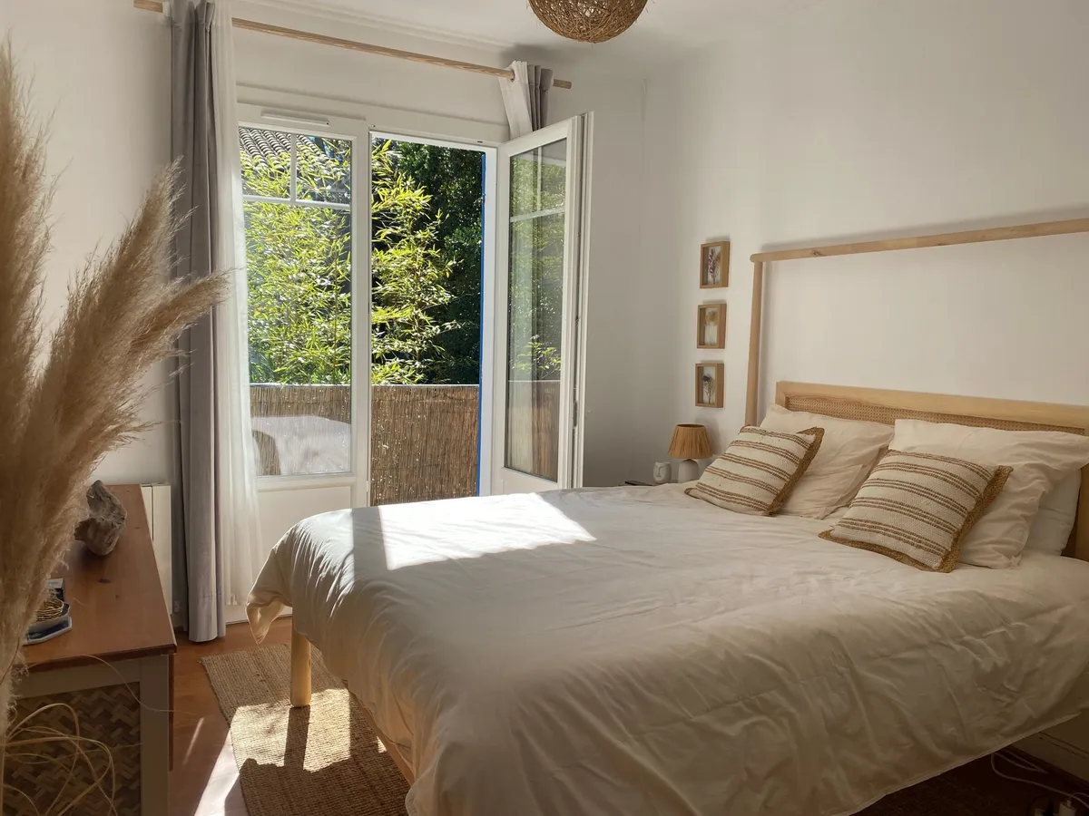 Chambre baignée de soleil, porte-fenêtre ouverte sur le jardin et gerbe de pampa