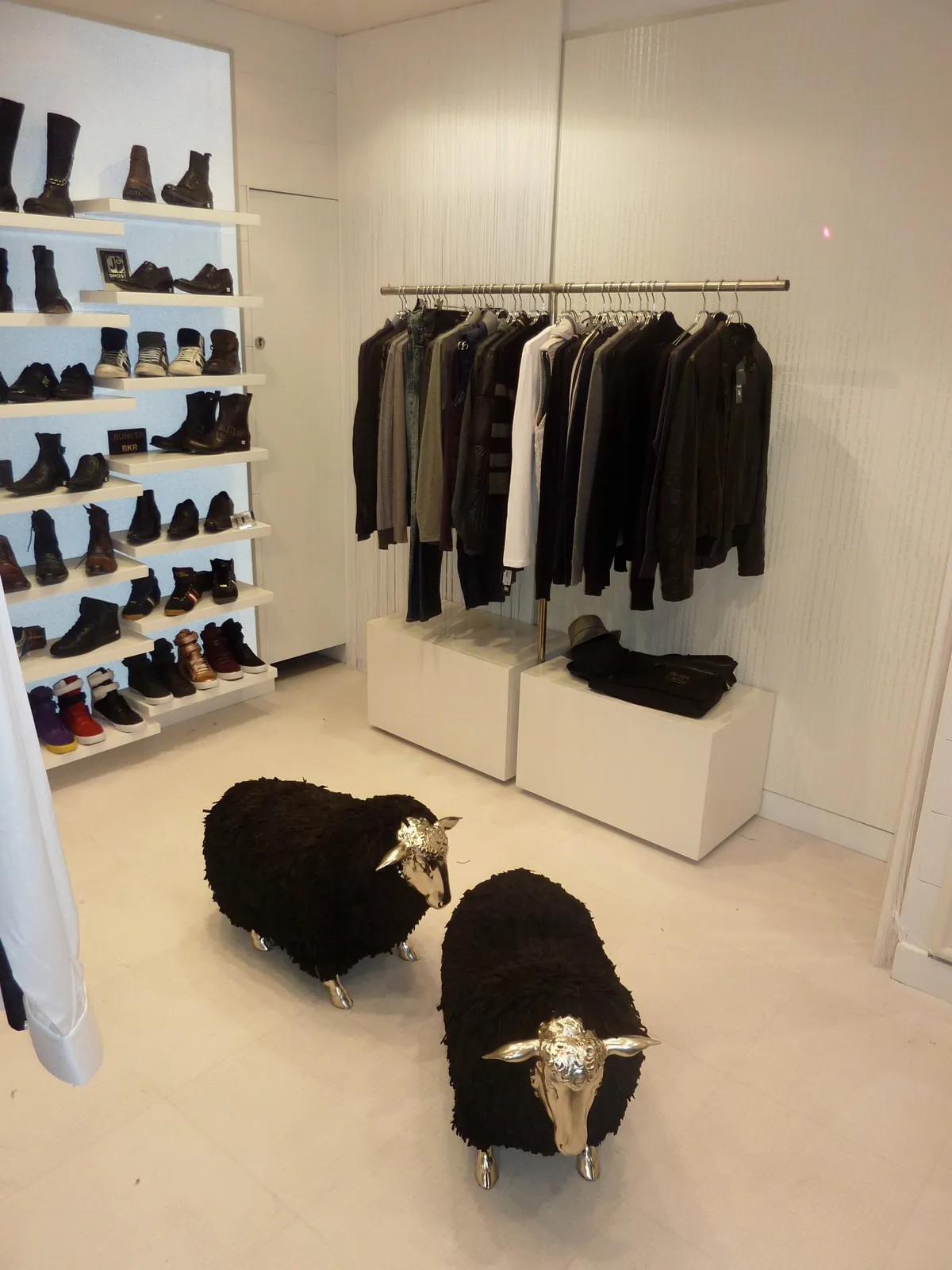 Boutique blanche, étagères à chaussures, portant de vêtements sombres et moutons sculptés