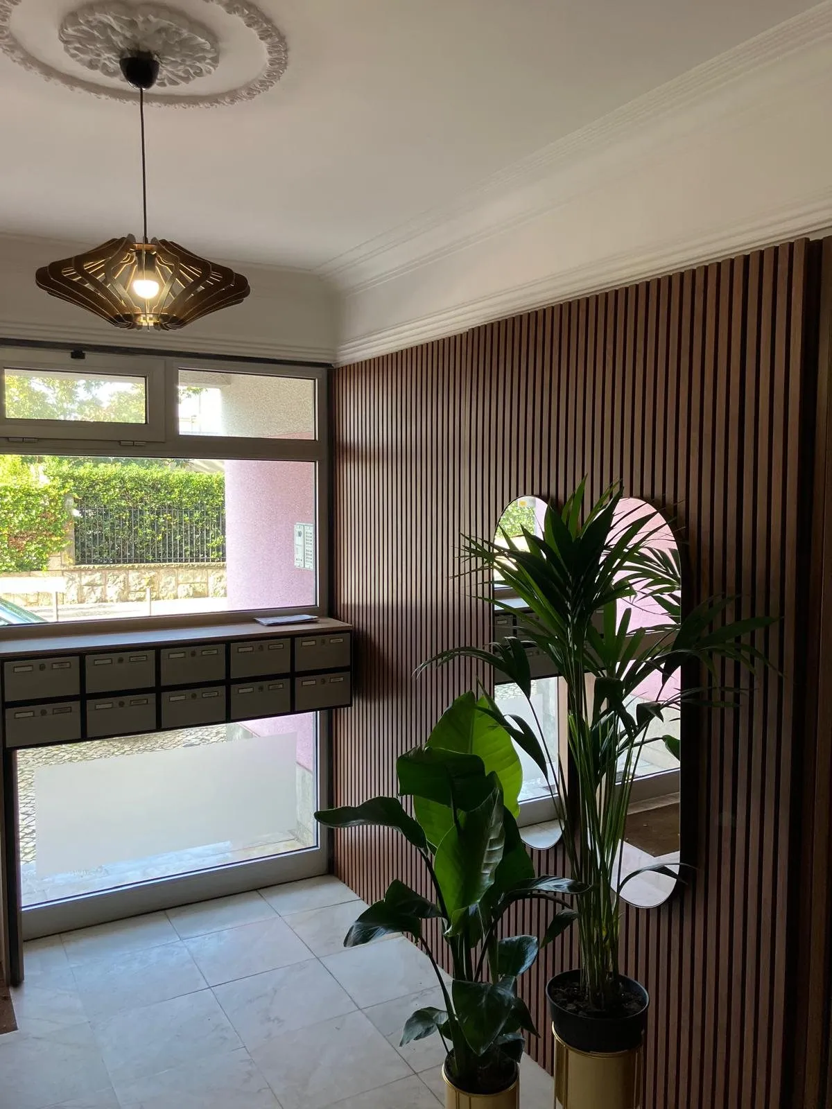 Hall habillé de tasseaux de bois, suspension ajourée, miroir arrondi et plantes vertes