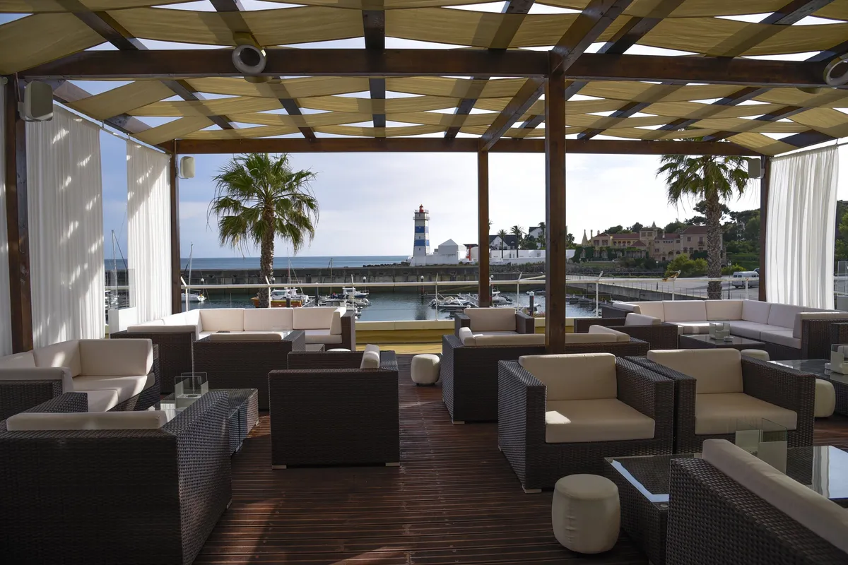 Terrasse sous pergola face à la marina, salons en résine tressée et coussins blancs