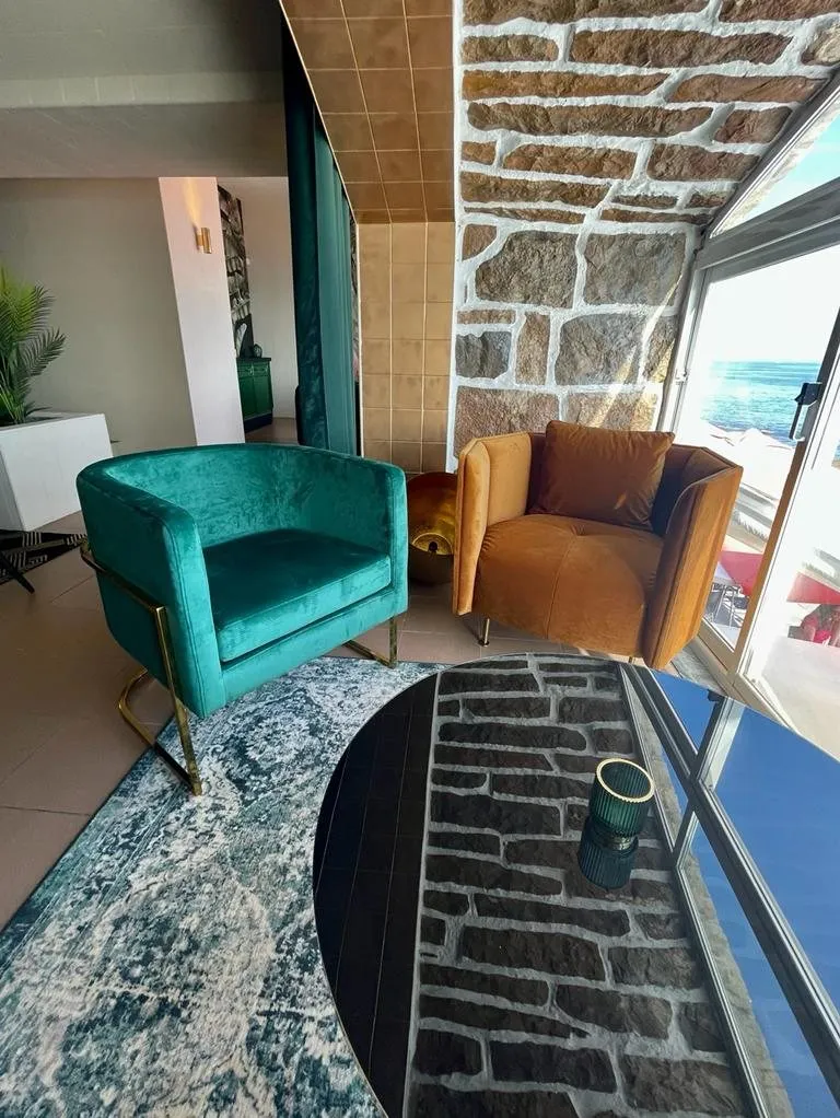 Fauteuils en velours vert et cognac devant une arche en pierre, sur un tapis bleu