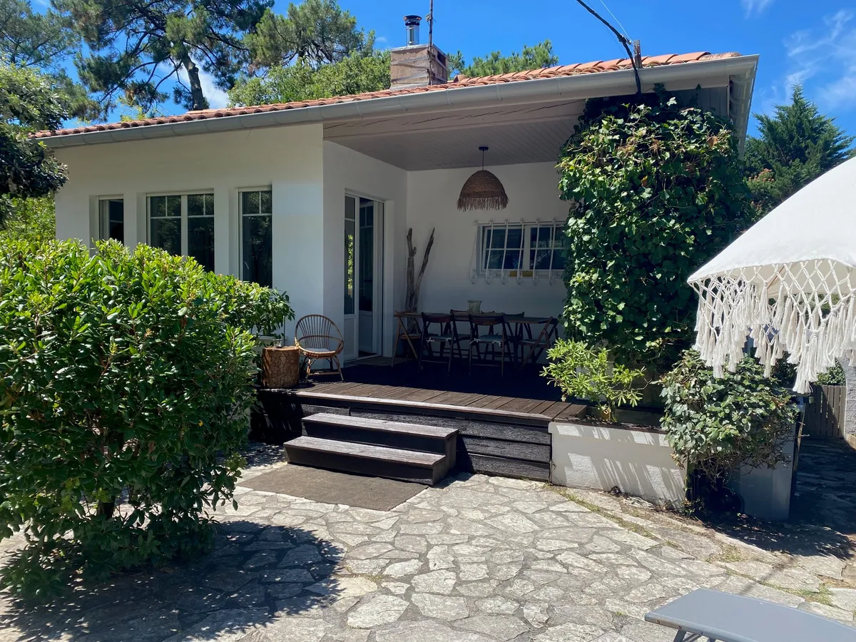 Maison blanche et sa terrasse en bois, entourées de verdure