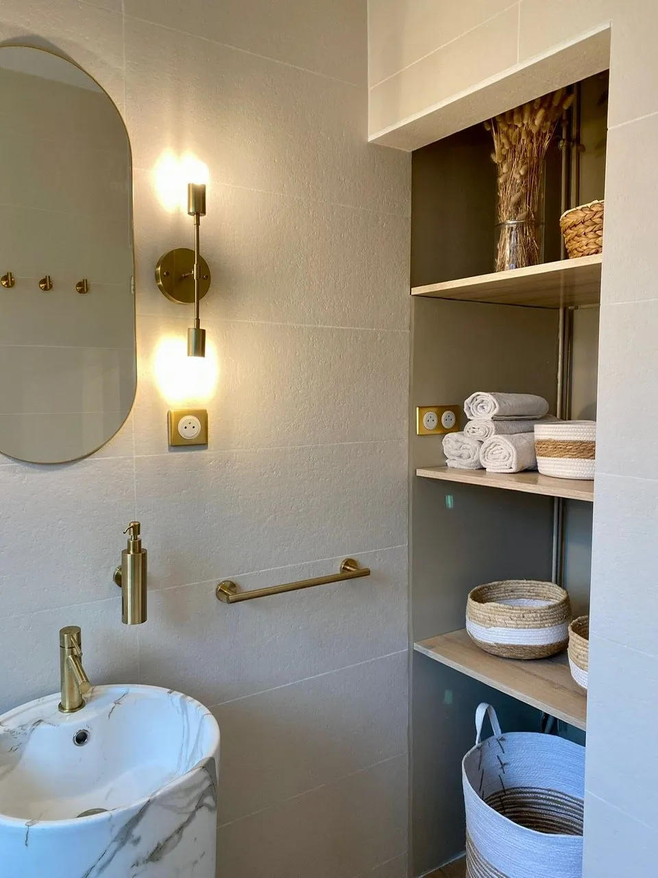 Miroir ovale, appliques dorées et niche d'étagères garnie de paniers tressés