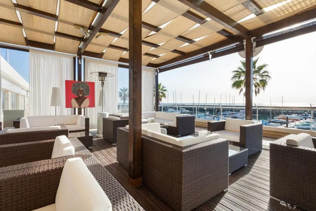 Salons de la terrasse sous la pergola en bois, ouverts sur la marina