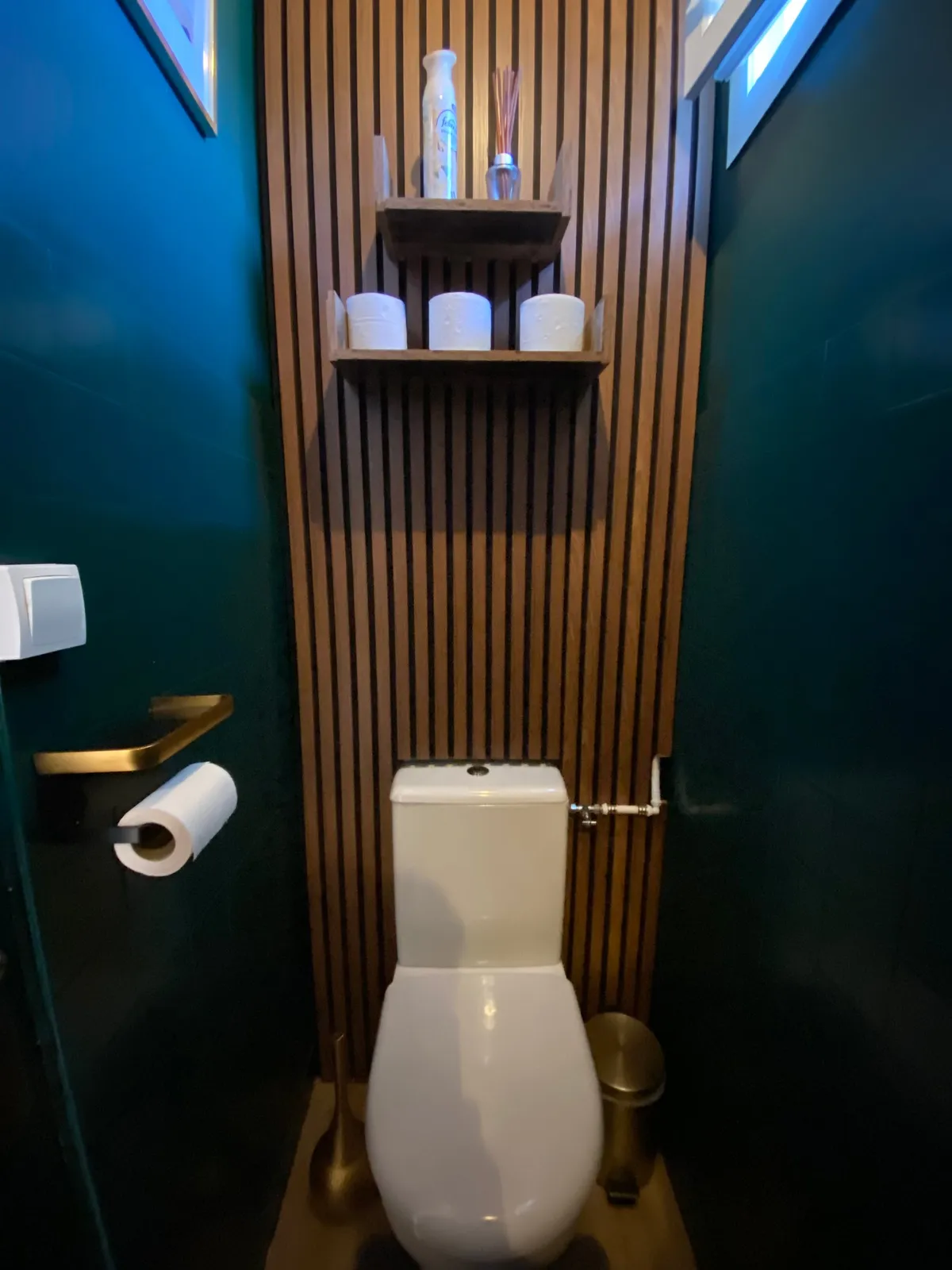 Toilettes habillées de tasseaux de bois sur un mur vert profond